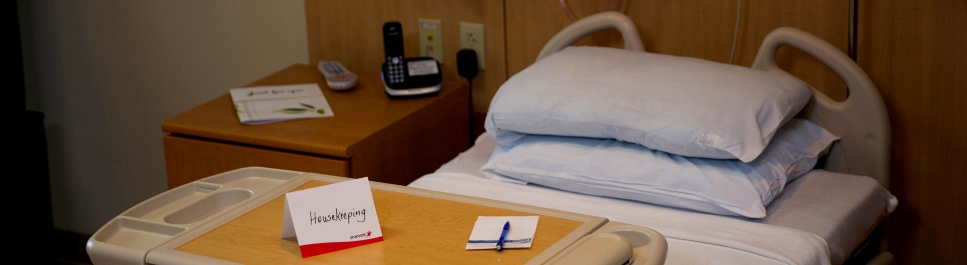 An empty hospital bed with a Housekeeping card folded on the tray table.